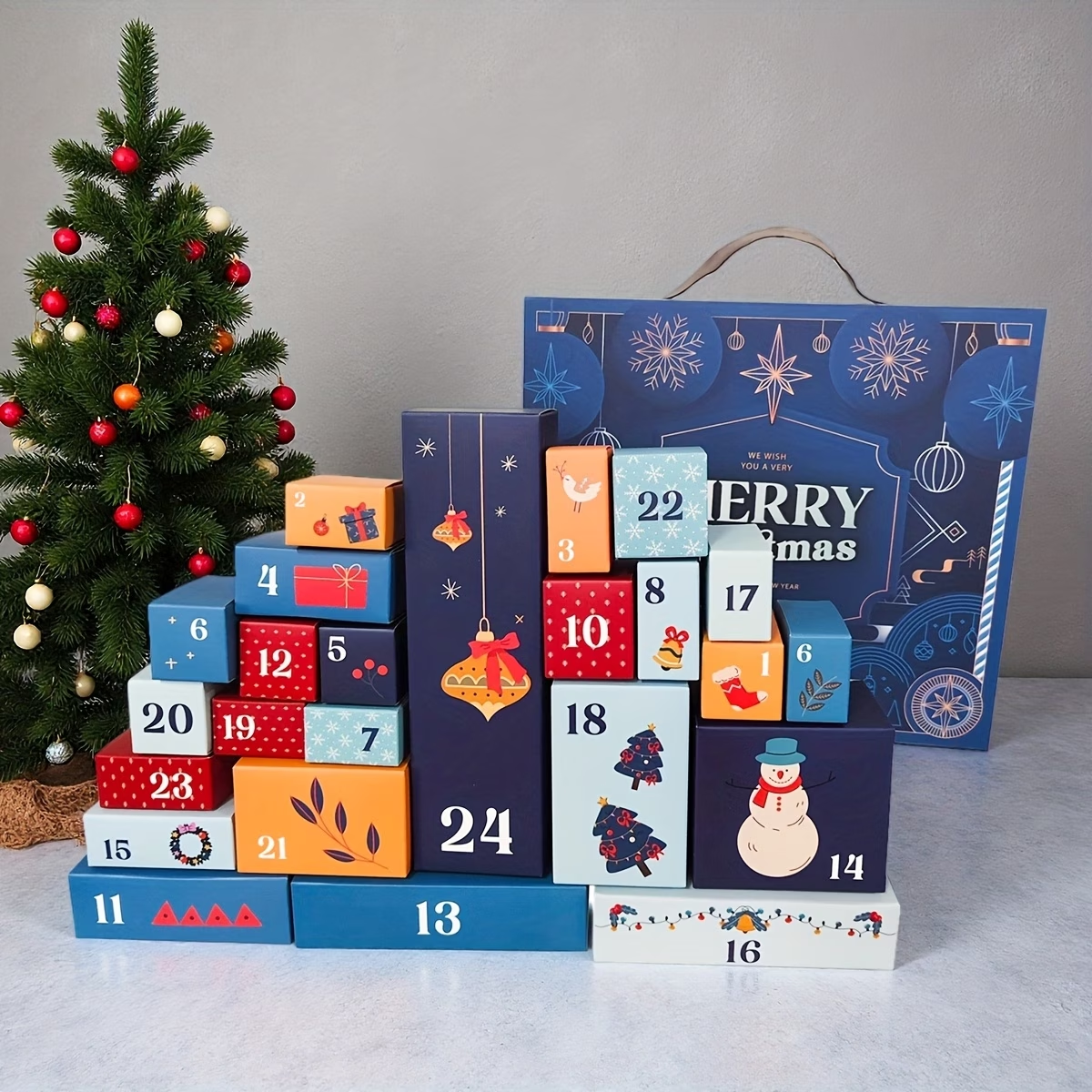 Tom adventskalender: tjugofyra numrerade småaskar i blått och rött staplade framför en julgran